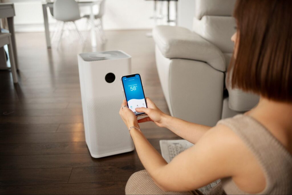 Woman checking indoor humidity levels on her smartphone while sitting near a portable air purifier in a modern living room.