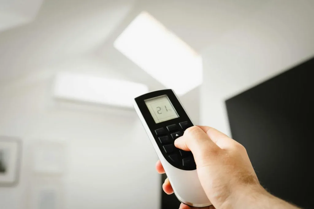 Person turning on air conditioner with remote highlighting risks of running AC without filter
